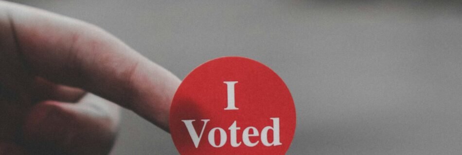 a hand holding a red button that says i vote